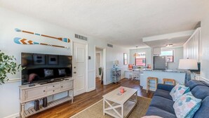 A modern living room with a flat-screen TV, wooden entertainment unit, and a cozy seating area with a sofa and coffee table. - Exquisite Rooftop Deck Beach View Pool Spacious (St. Pete Beach)