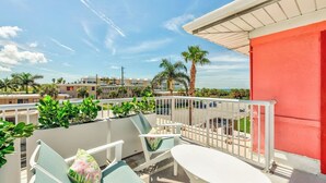 A balcony with outdoor seating, a red wall, and a view of the surrounding buildings and palm trees. - Exquisite Rooftop Deck Beach View Pool Spacious (St. Pete Beach)