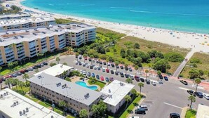 A coastal hotel with multiple buildings, a parking lot, and a beach in the background.