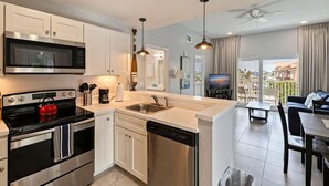 A modern kitchen with stainless steel appliances, a dishwasher, and a dining area with a view. - Madeira Beach Condo |Walk to Beach|Johns Pass|Pool (Madeira Beach)