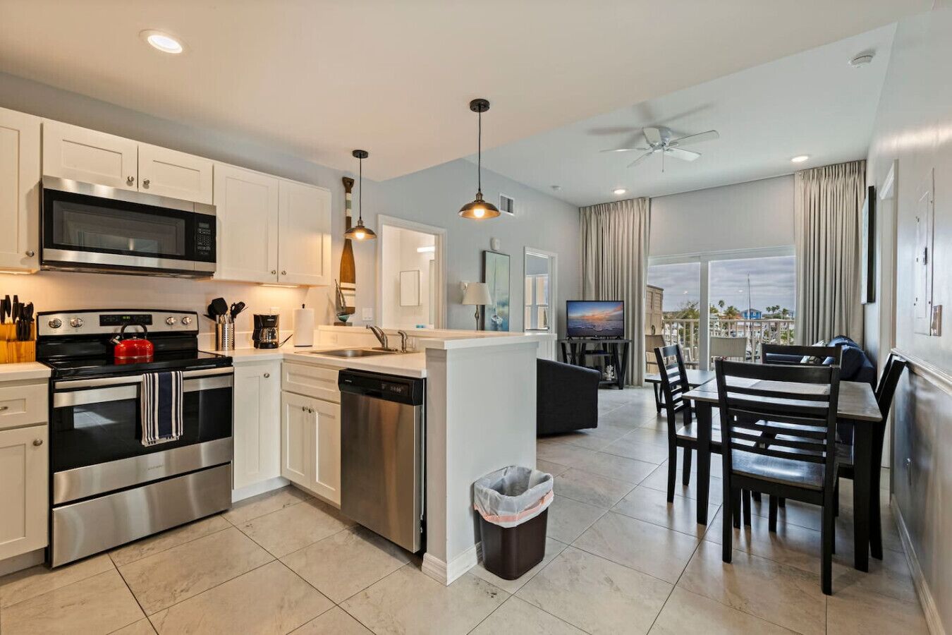 A modern kitchen with stainless steel appliances, a dining area with a view, and a balcony with curtains.