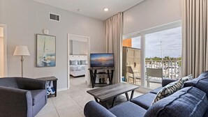 A modern living room with a sofa, a TV, and a balcony with a view of the marina. - Madeira Beach Condo |Walk to Beach|Johns Pass|Pool (Madeira Beach)