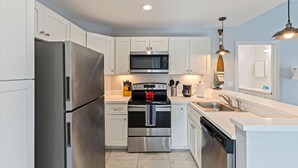A modern kitchen with stainless steel appliances, white cabinetry, and a central island. - Madeira Beach Condo |Walk to Beach|Johns Pass|Pool (Madeira Beach)
