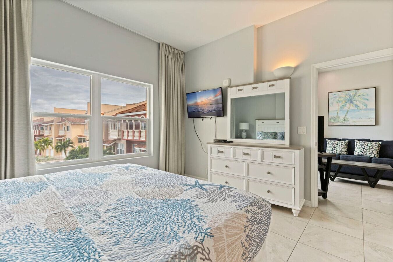 A hotel room with a large bed, a TV, a dresser, and a view of buildings outside.