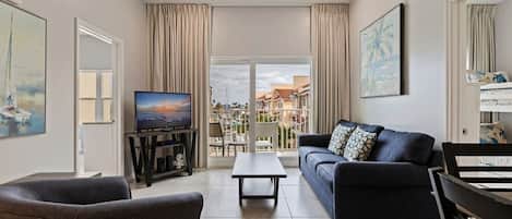 Ein Wohnzimmer mit einer Couch, einem Fernseher und Blick auf einen Balkon mit Gartenmöbeln.