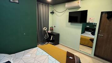 Un dormitorio con cama, escritorio, silla, espejo y aire acondicionado.