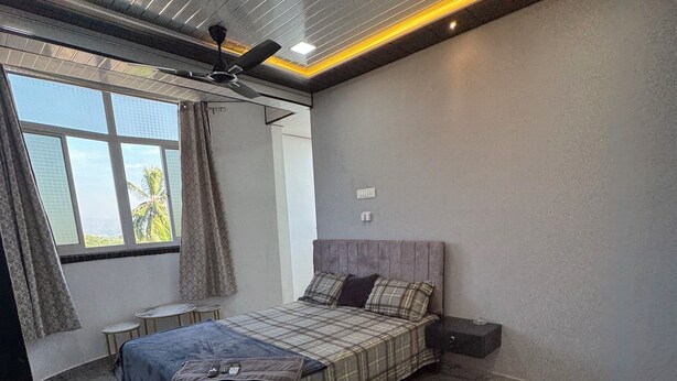 Une chambre à coucher comprenant un lit, une table de chevet, une fenêtre avec des rideaux, un ventilateur de plafond et une vue sur des palmiers.