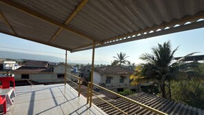 Un espace extérieur abrité, doté d’un sol carrelé, d’un escalier et offrant une vue sur les bâtiments environnants et les palmiers.
