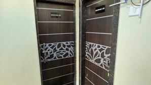 Deux portes en bois sombre, ornées de motifs décoratifs, portant les inscriptions « SALLE N° 04 » et « SALLE N° 05 », se trouvent dans un couloir dont le sol est recouvert de carreaux et où l’on aperçoit une petite portion de gazon artificiel.