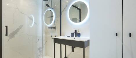 Une salle de bain moderne avec une douche à parois de verre, un meuble-lavabo avec un miroir et un pare-baignoire en marbre.