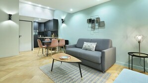 Un salon moderne avec un canapé gris, une table basse, un coin repas avec des chaises et une cuisine en arrière-plan.