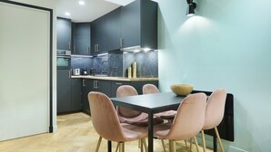Une cuisine moderne avec des meubles de couleur sombre, un pare-feu en marbre et un coin repas comprenant une table noire et des chaises roses.