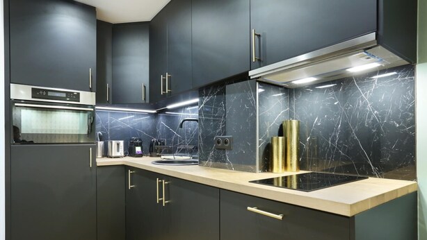 Une cuisine moderne avec des meubles de couleur sombre, un pare-feu en marbre et des appareils électroménagers en acier inoxydable.