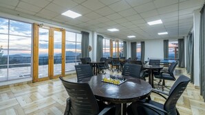 A spacious conference room with large windows, a chessboard on the table, and multiple chairs. - Nirvana Dhar Nature Resort (Rajgarh)