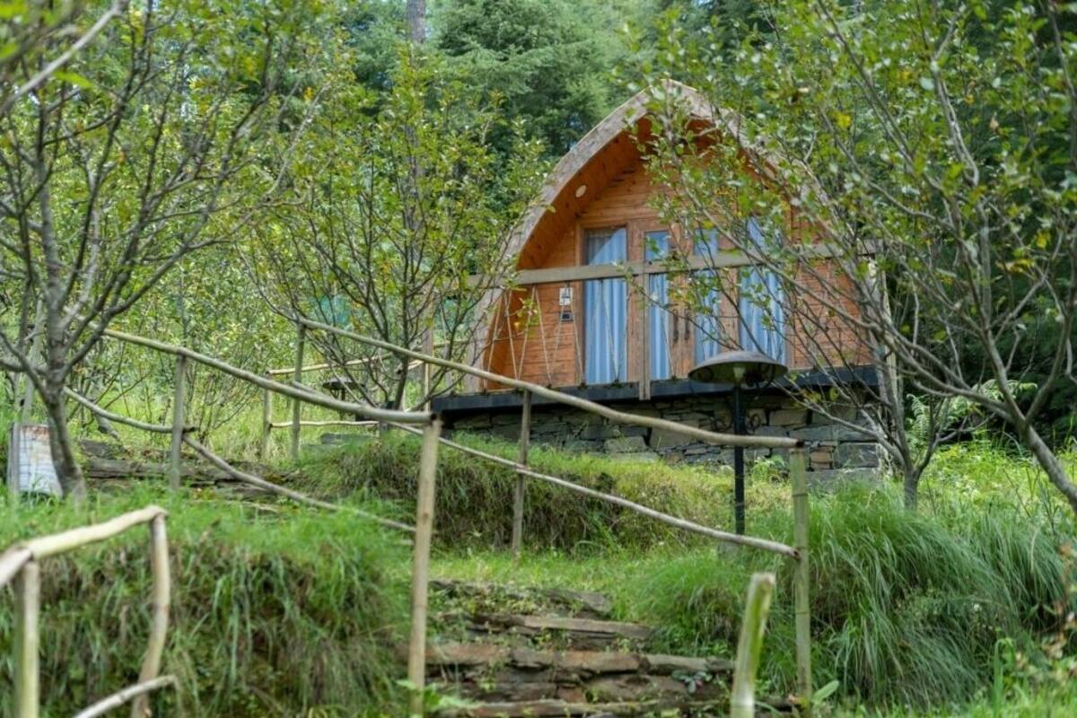 Una cabaña rústica con cimientos de piedra, rodeada de exuberante follaje y un puente de madera que lleva a ella.