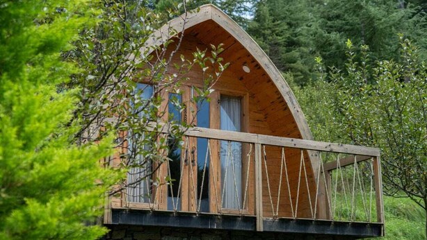 A wooden cabin with a stone foundation, large windows, and a balcony with rope railings. - Nirvana Dhar Nature Resort (Rajgarh)