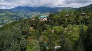A mountainous landscape with a prominent house surrounded by dense forest. - Nirvana Dhar Nature Resort (Rajgarh)