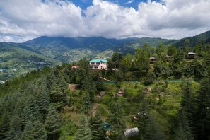 A mountainous landscape with a prominent house surrounded by dense forest. - Nirvana Dhar Nature Resort (Rajgarh)
