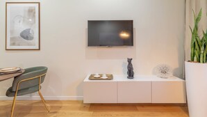 A modern living room with a flat-screen TV mounted on the wall, a green chair, a white console table with a cat figurine, and a potted plant. - New apartment in central Rome, close to subway, full equiped, king bed, Wifi. (Roma)