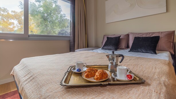 A neatly made bed with a tray of croissants, a cup of coffee, and a teapot on a window-side table. - New apartment in central Rome, close to subway, full equiped, king bed, Wifi. (Roma)
