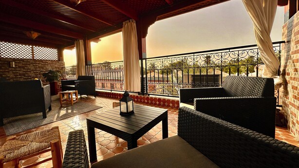 A balcony with wicker furniture, a table, and a view of the cityscape. - Authentic Riad Dar Adam / Splendid Rooftop & Pool (Marrakech)