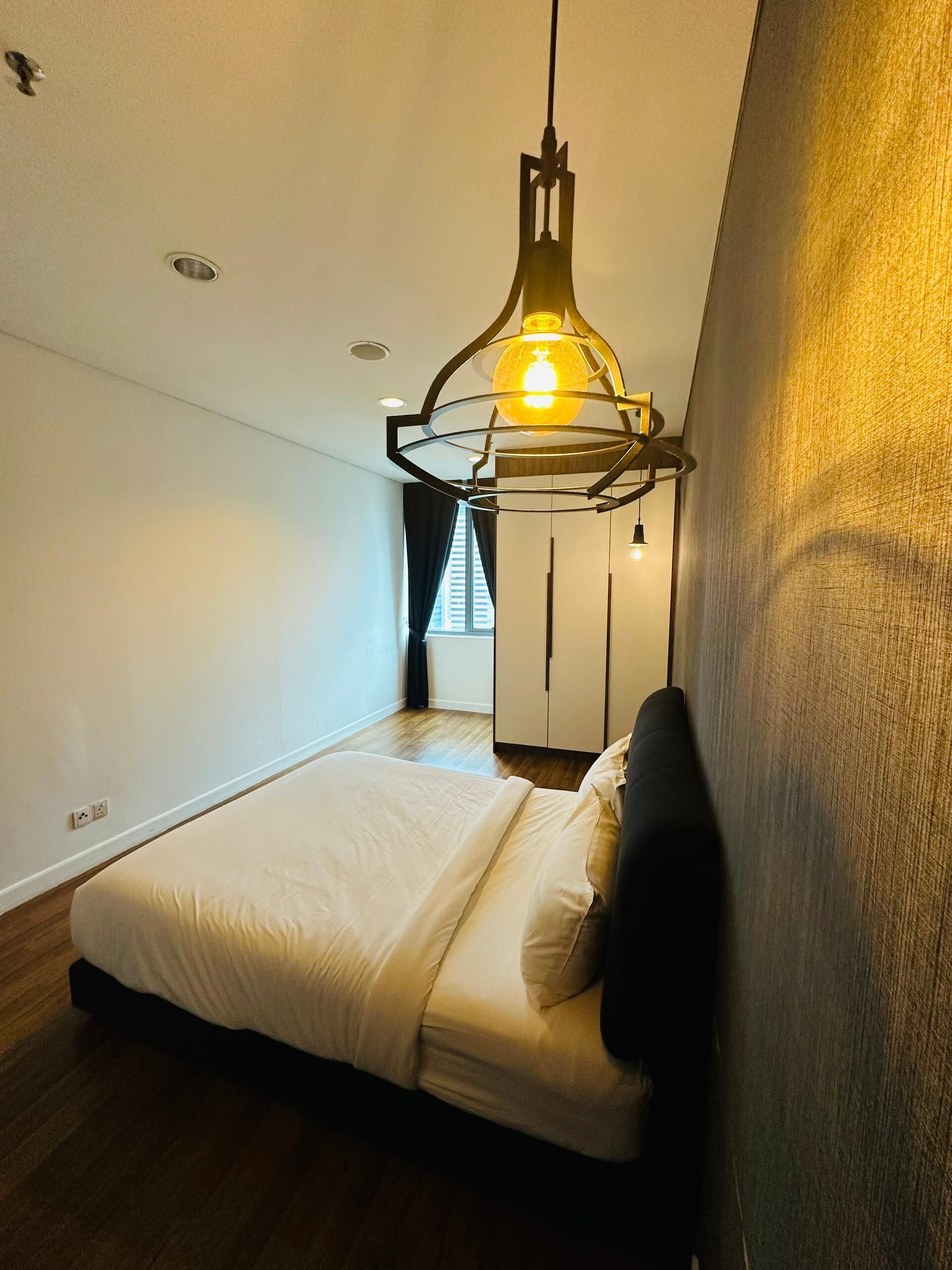 A modern bedroom with a bed, a hanging light fixture, and a wardrobe.