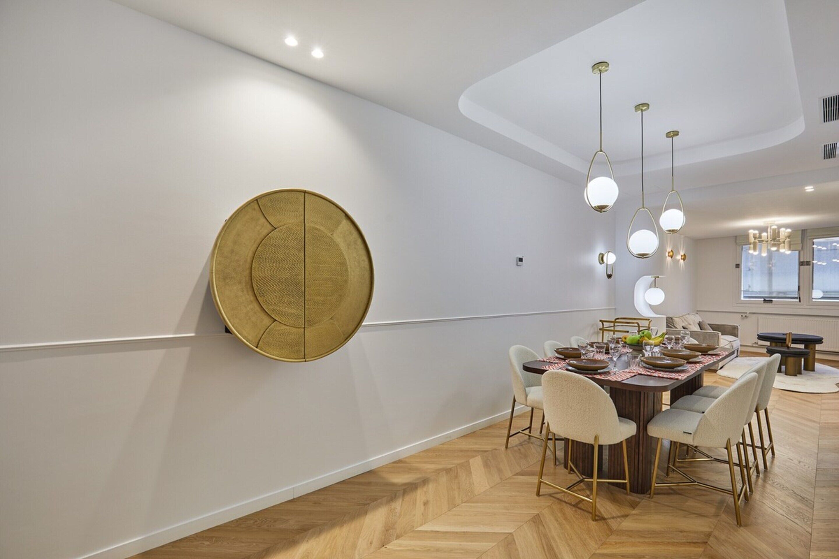 Een moderne eetruimte met een visgraatparketvloer, een ronde gouden accentmuur en een eettafel gedekt voor zes personen met witte stoelen.