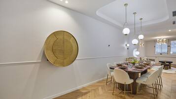 Een moderne eetruimte met een visgraatparketvloer, een ronde gouden accentmuur en een eettafel gedekt voor zes personen met witte stoelen.