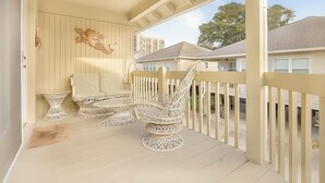 Een overdekt terras met rieten meubels, een decoratief object aan de wand en uitzicht op omliggende gebouwen.