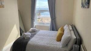 Un lit bien fait, recouvert d’une couette blanche et grise, avec un oreiller jaune et un plaid gris.