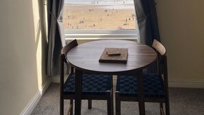 Une pièce avec vue sur la plage, une table ronde avec deux chaises et une fenêtre avec des rideaux.