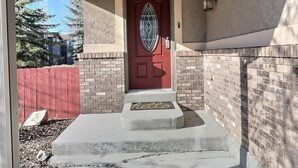 Una entrada de casa con puerta roja, un pequeño porche y un muro de ladrillo.