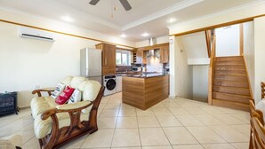 A spacious living area with a sofa, a wooden coffee table, a ceiling fan, and a kitchen area with wooden cabinets and a central island.