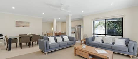 A modern living room with two grey sofas, a wooden coffee table, and a dining area with a table and chairs.