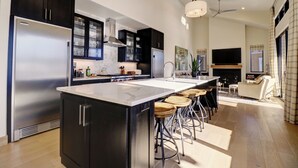 Una cocina moderna con una isla grande, taburetes de bar y una zona de comedor con sofá y televisor.
