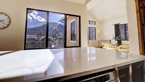 Una cocina con un ventanal amplio, un reloj y vistas a montañas.