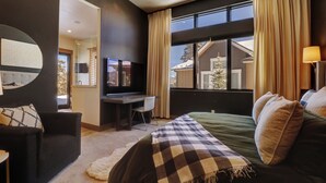 Una habitación de hotel moderna con una cama grande, un escritorio, un televisor y vistas a un paisaje nevado.
