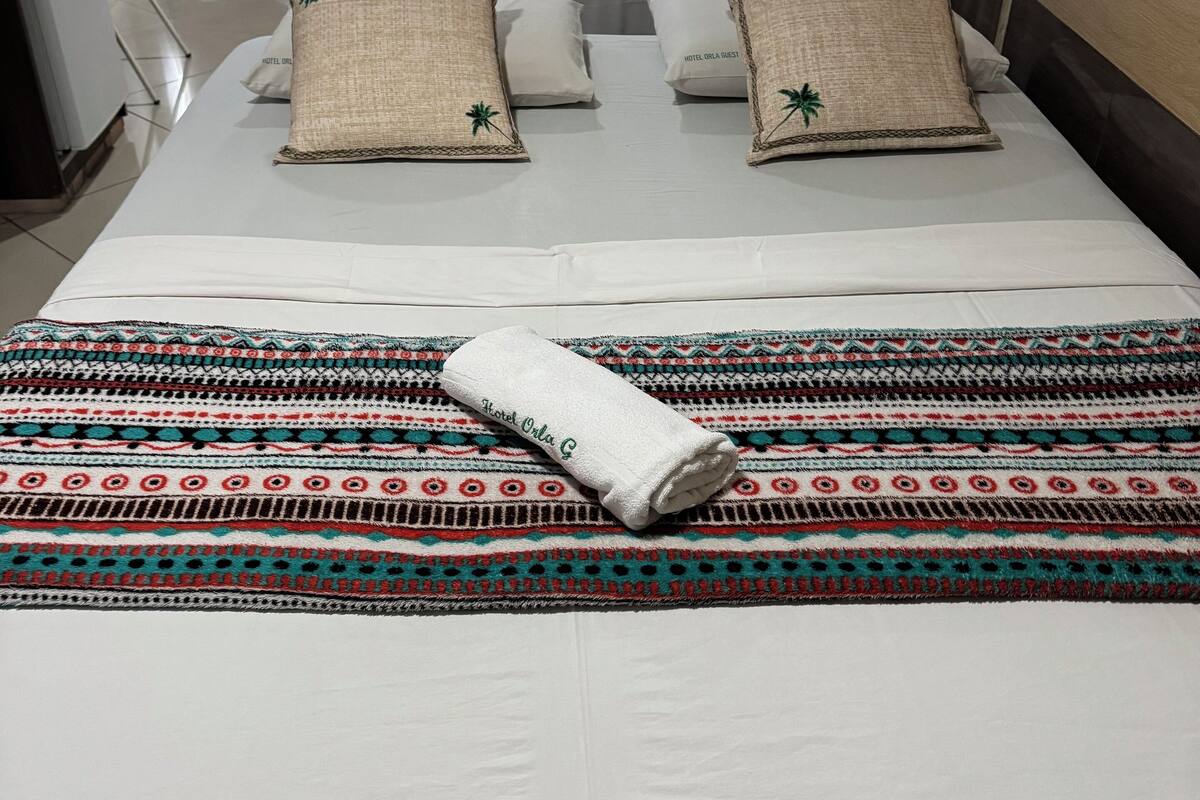 A neatly made bed with a patterned blanket, two decorative pillows, and a folded towel.