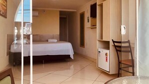 A hotel room with a bed, a small table, a chair, a mini-fridge, and a wardrobe. - Hotel orla Guest House (Petrolina)