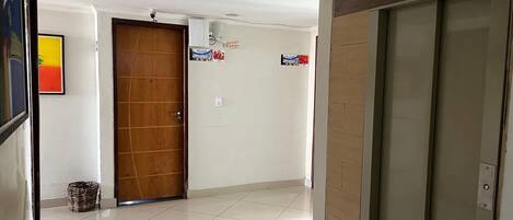 A hallway with a wooden door, a tiled floor, and a wall-mounted air conditioning unit.