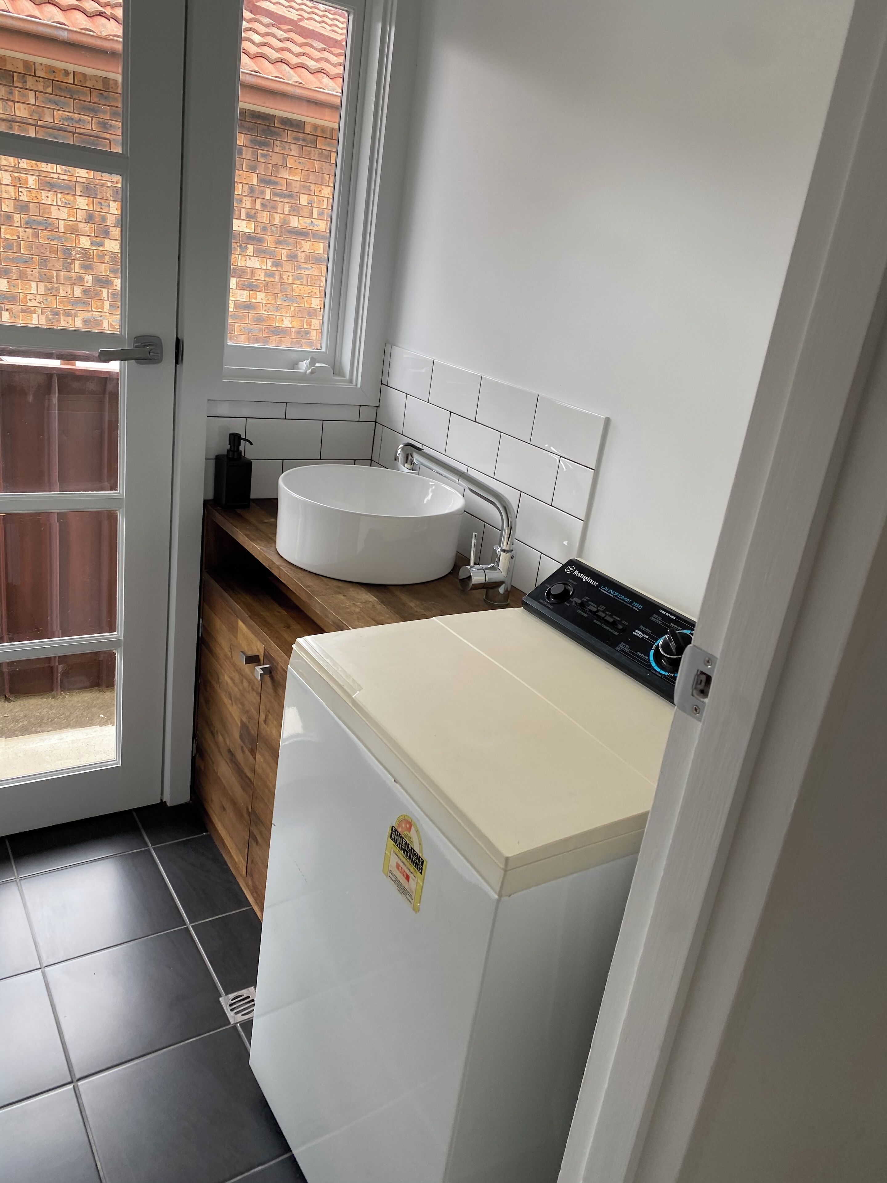 Una cocina compacta con un lavamanos, lavadora y ventana.
