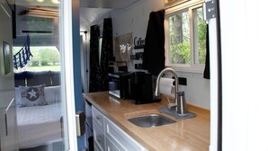 A compact kitchen with a sink, coffee maker, and a window with curtains.