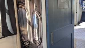 A room with a shower curtain featuring a reflective metallic design, a blue door with a small window, and a bed with a quilted white cover.