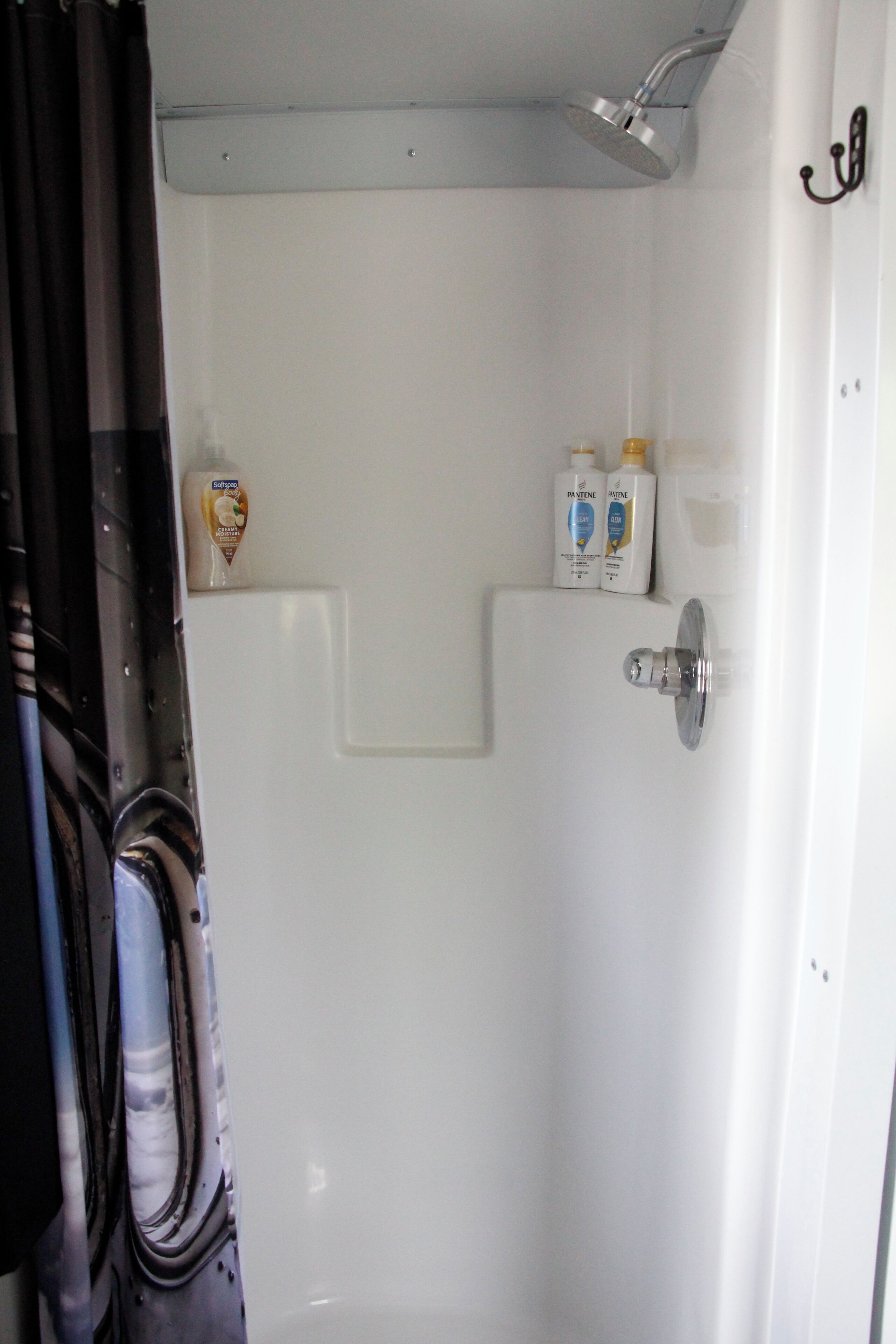 Un box de ducha blanco con un cabezal de ducha y un grifo. Hay dos botellas de jabón de manos en la pared.