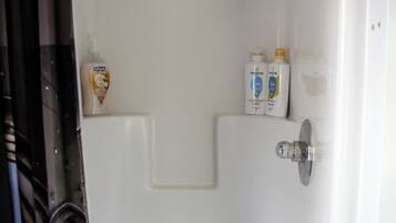 Un box de ducha blanco con un cabezal de ducha y un grifo. Hay dos botellas de jabón de manos en la pared.