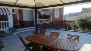 A covered patio with a wooden table and chairs, a bench, and a railing. - DALI HOLIDAY HOME 5 minutes from the sea and the cetacean sanctuary (Imperia)