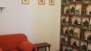 A room with a red sofa, a small wooden table, and a bookshelf filled with books and plants. - DALI HOLIDAY HOME 5 minutes from the sea and the cetacean sanctuary (Imperia)