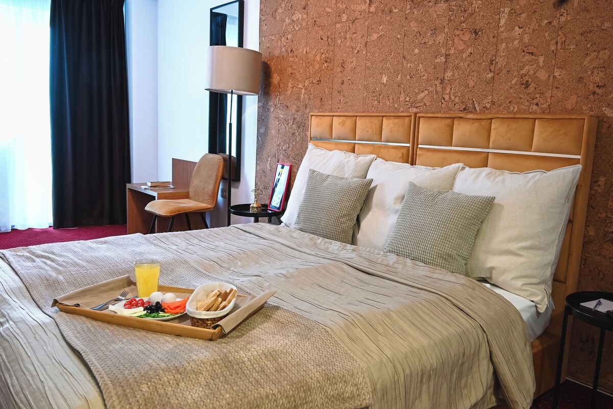 Ett hotellrum med en säng, ett brickbord med frukost, en stol, en lampa och en vägg med ett mönstrat ytskikt.