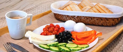A tray with a plate of food including tomatoes, cucumbers, cheese, eggs, olives, and bread, along with a cup of coffee.