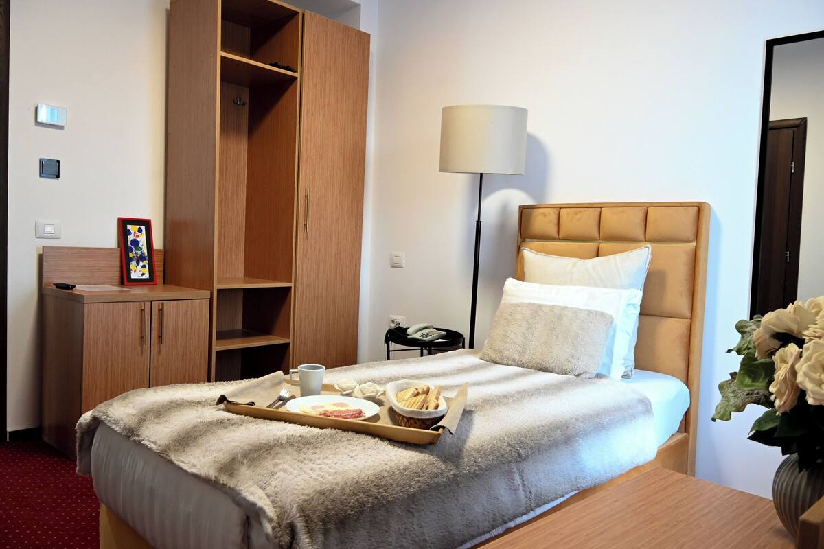 A hotel room with a bed, a bedside table, a lamp, a wardrobe, and a tray with breakfast items.
